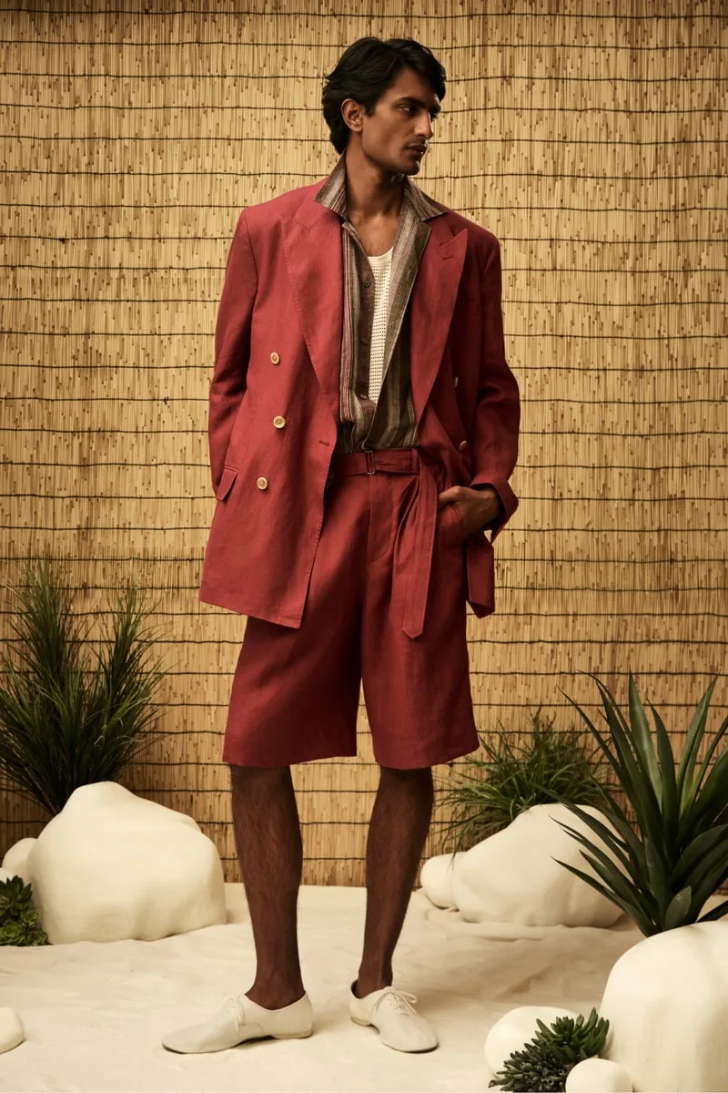 Homme portant un costume rouge et des chaussures blanches, fond de bambou.