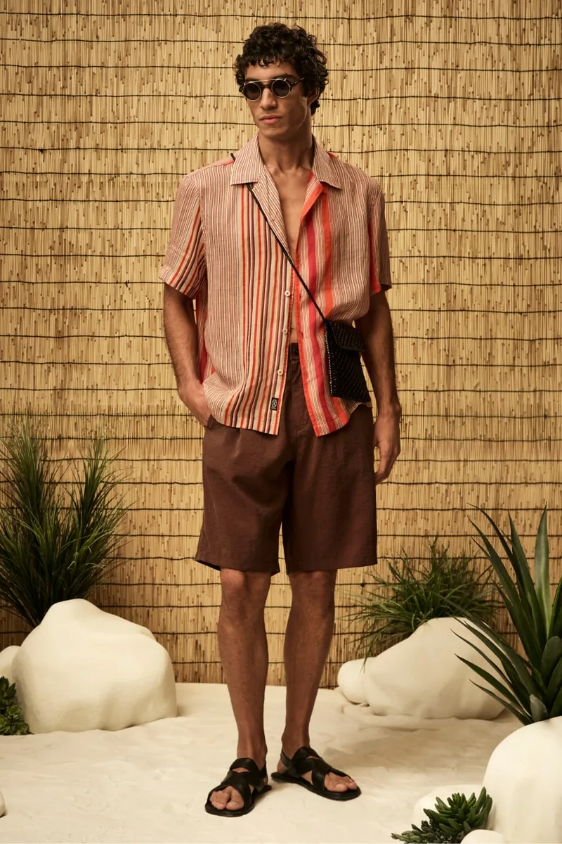 Homme en chemise rayée et short, portant des lunettes de soleil.
