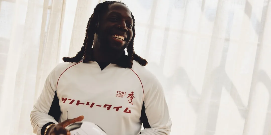 Homme souriant en maillot blanc, tenant un ballon, lumière naturelle en arrière-plan.