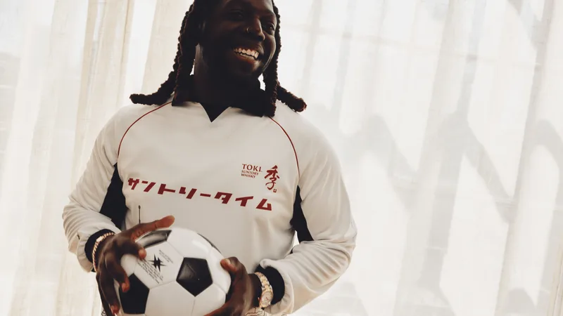 Homme souriant avec un ballon de football, portant un maillot blanc.