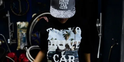 Personne portant casquette et t-shirt 'Tokyo Drive Car Club' dans garage.