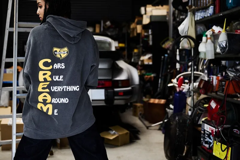 Personne avec sweat à capuche dans un garage rempli d'objets et voitures.