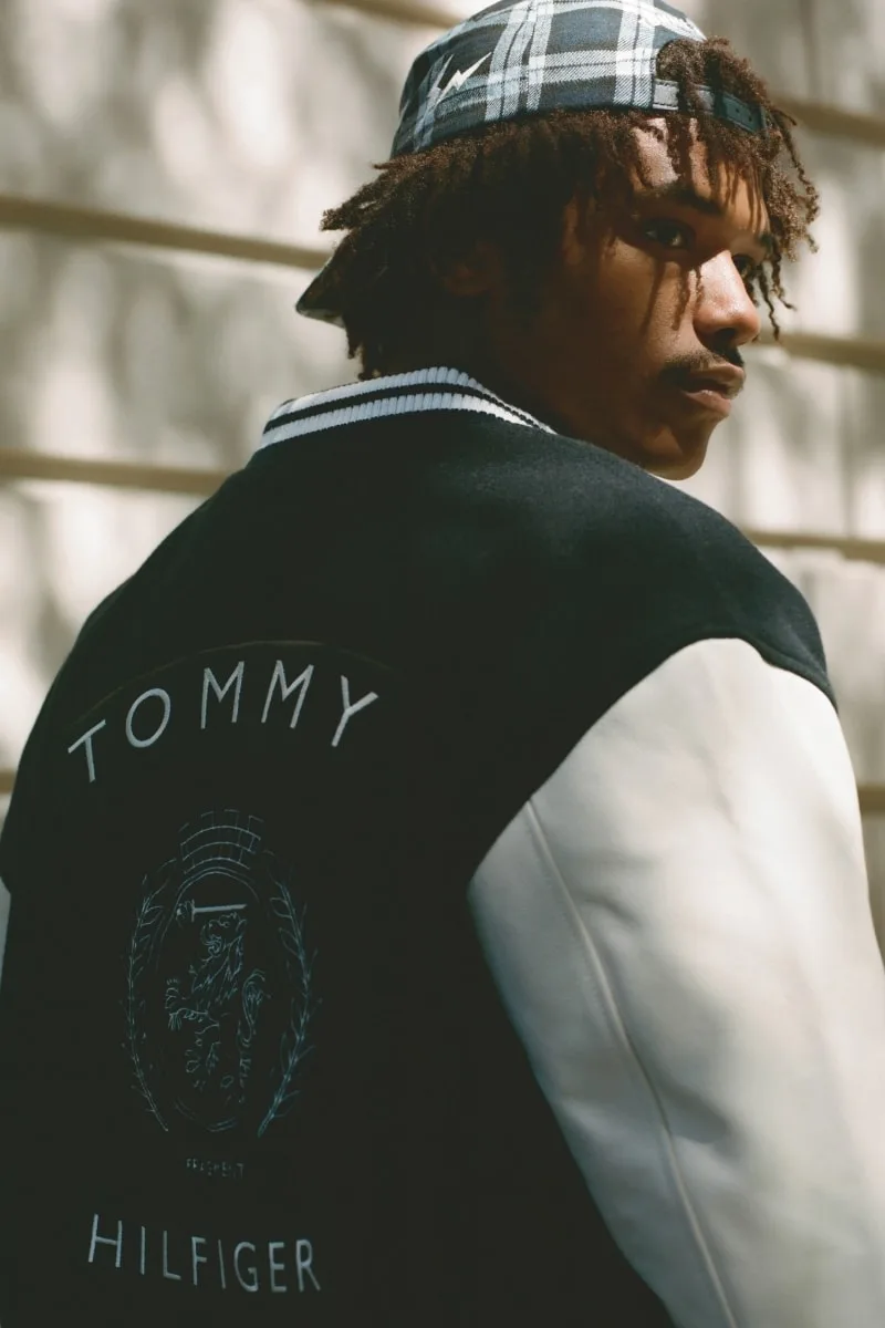 Homme en veste Tommy Hilfiger avec casquette et cheveux bouclés.