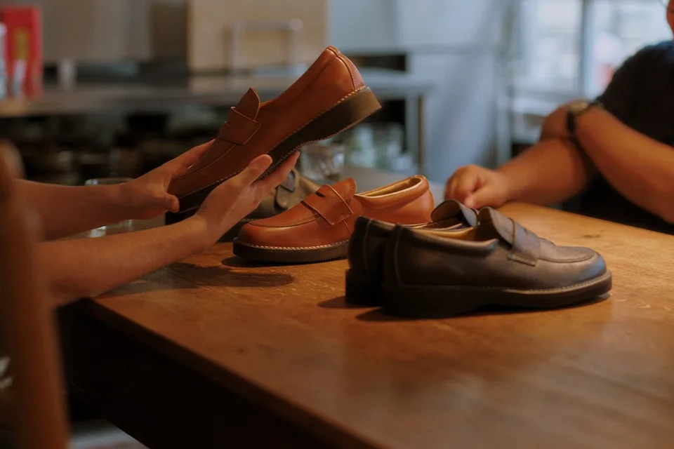 Deux personnes examinent des chaussures en cuir sur une table en bois.