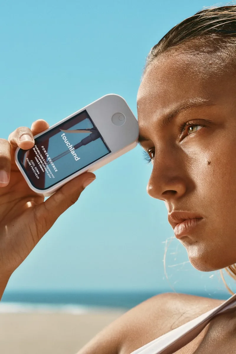 Femme tenant un appareil sur son front à la plage, ciel bleu en arrière-plan.