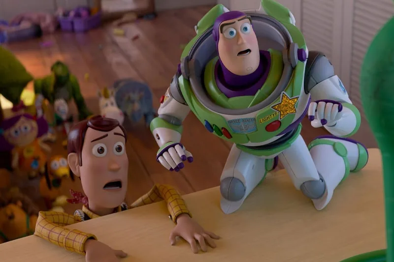 Woody et Buzz Lightyear regardent vers le haut dans une pièce encombrée.