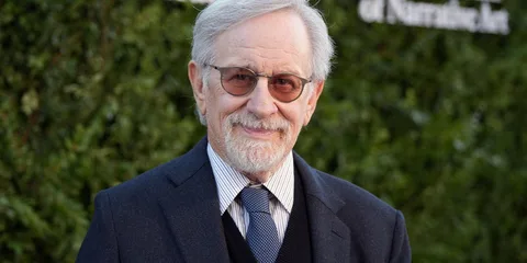 Homme âgé souriant, portant des lunettes et un costume.