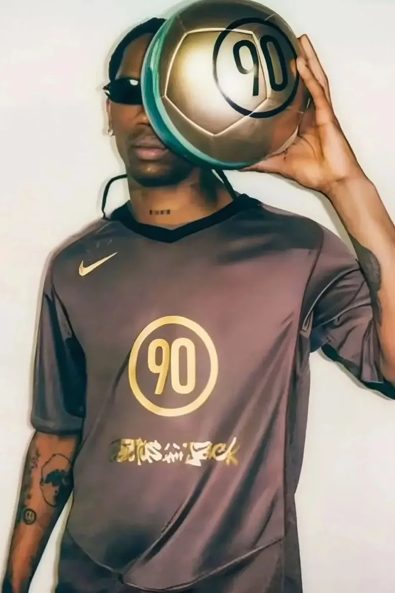 Homme avec un maillot marron portant un ballon doré marqué '90'.
