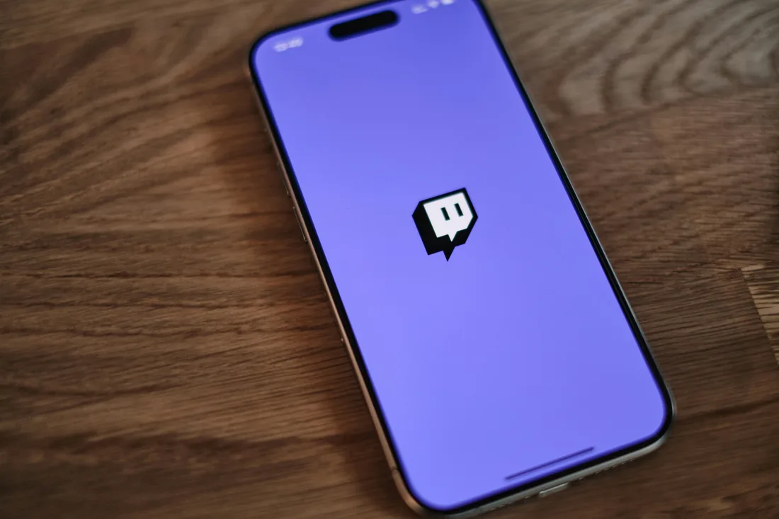 Smartphone affichant le logo de Twitch sur fond violet, posé sur un bureau en bois.
