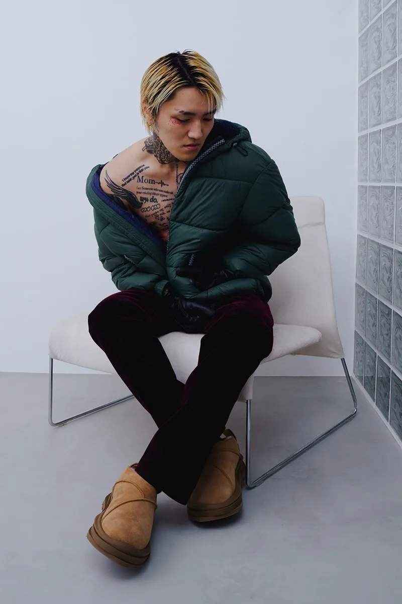 Homme assis sur une chaise, veste verte et pantoufles beige.