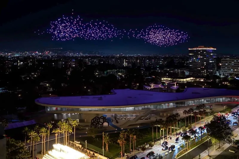 Vue nocturne d'une ville avec spectacle lumineux dans le ciel et bâtiment moderne.