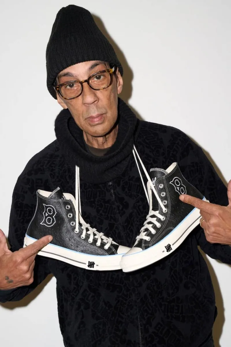 Homme avec des baskets noires, fond blanc, bonnet noir.
