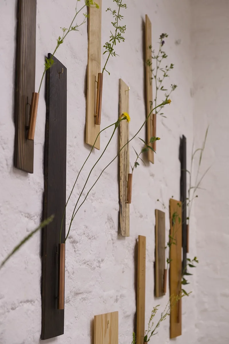 Planches en bois avec fleurs fixées, accrochées à un mur blanc.