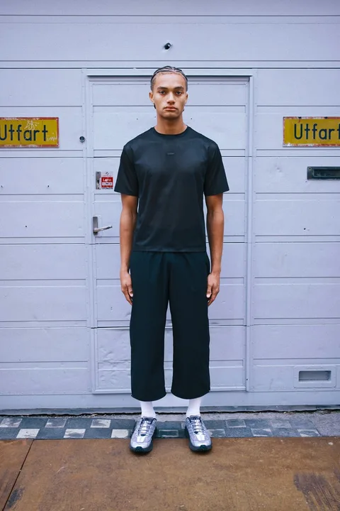 Homme debout en vêtements noirs devant une porte grise.