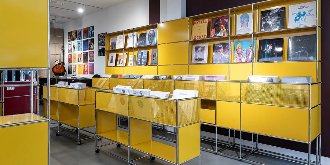Magasin de disques avec étagères jaunes et pochettes d'albums exposées.