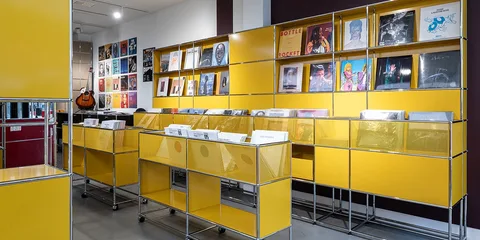 Magasin de disques avec étagères jaunes et pochettes d'albums exposées.