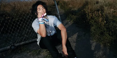 Jeune homme assis près de clôture avec bracelets colorés.