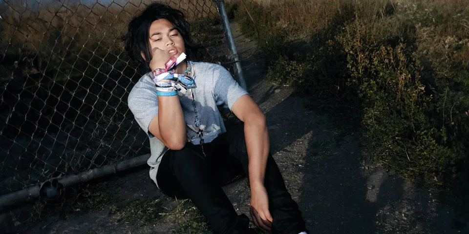 Jeune homme assis près de clôture avec bracelets colorés.