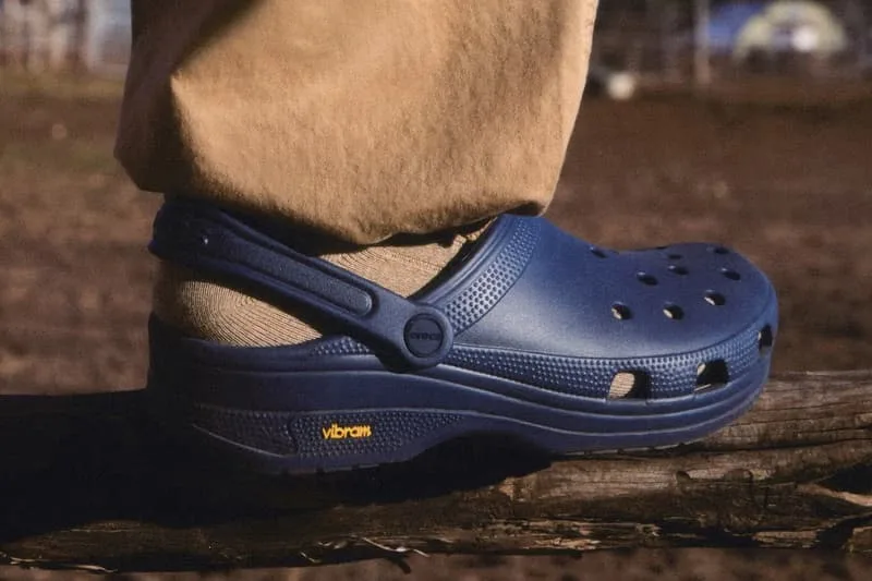 Sabot bleu avec semelle Vibram et pantalon beige sur une branche en bois.
