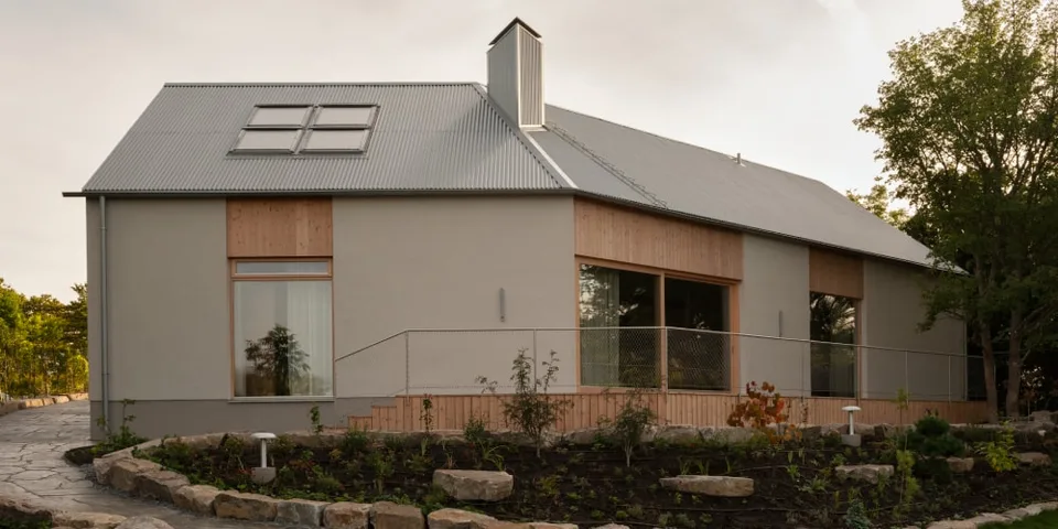 Maison moderne avec toit en métal et grands panneaux vitrés.