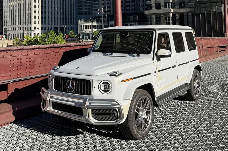 SUV Mercedes blanc sur un pont en métal dans une ville.