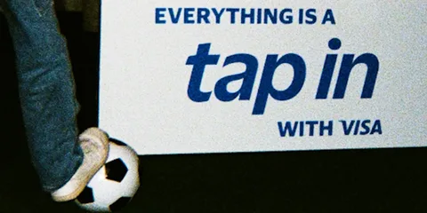 Pied sur un ballon de football à côté d'une affiche 'EVERYTHING IS A tap in WITH VISA'.