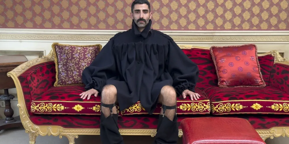 Homme assis sur un canapé luxueux en tenue noire excentrique.