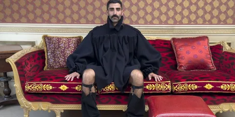 Homme assis sur un canapé luxueux en tenue noire excentrique.