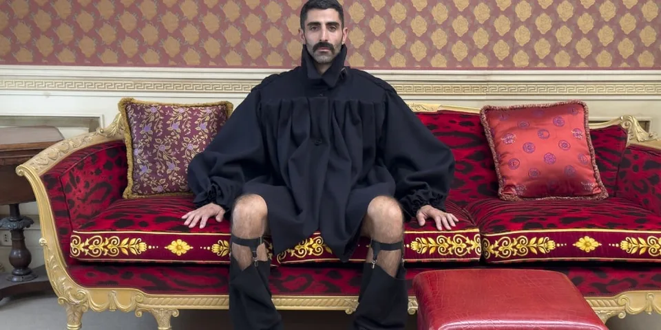 Homme assis sur un canapé luxueux en tenue noire excentrique.