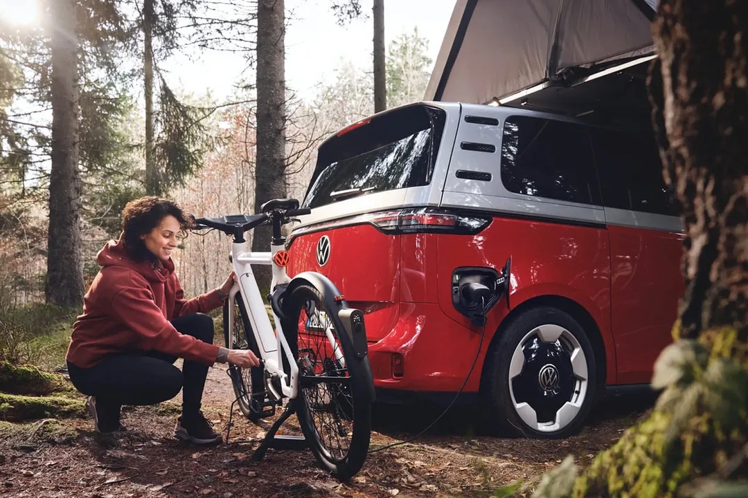 Personne charge un vélo électrique près d'un van parqué dans une forêt.