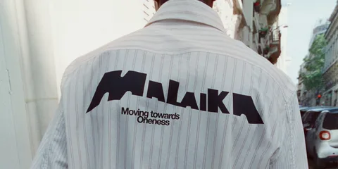Personne portant une chemise avec 'MALAIKA' écrit dessus dans la rue.