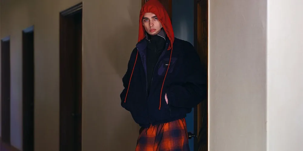 Personne en manteau noir et capuche rouge debout dans un couloir.