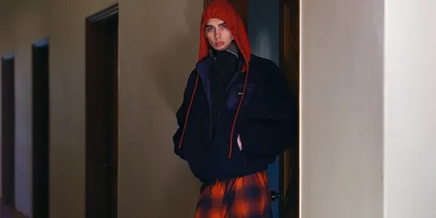 Personne en manteau noir et capuche rouge debout dans un couloir.