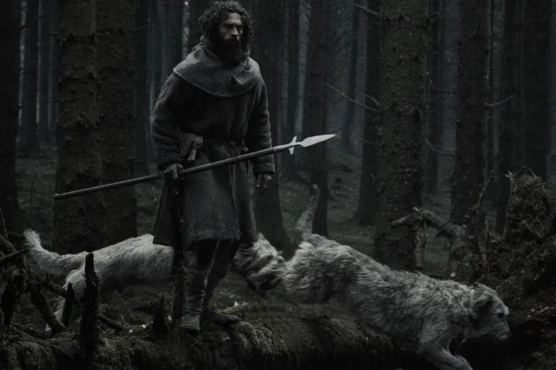 Homme avec lance dans une forêt sombre avec deux animaux ressemblant à des loups.