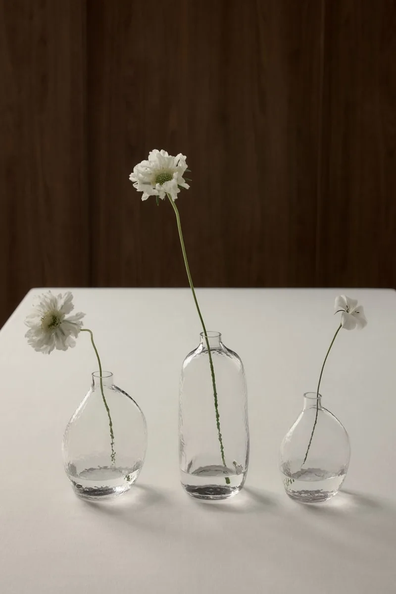 Trois vases en verre avec des fleurs blanches sur une table blanche.