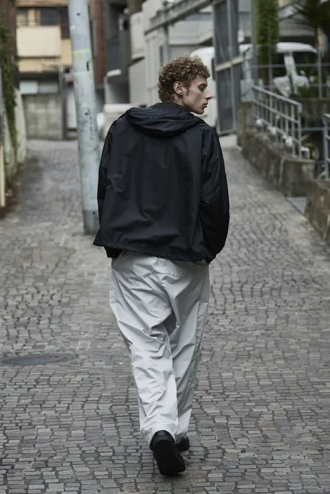Homme en veste noire et pantalon blanc marchant sur une rue pavée.