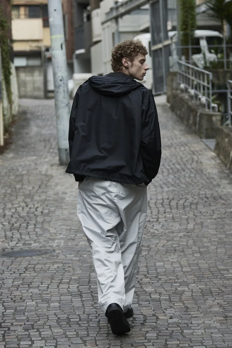 Homme en veste noire et pantalon blanc marchant sur une rue pavée.