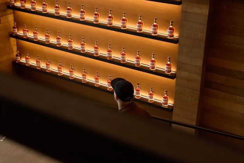 Homme avec casquette devant des étagères de bouteilles illuminées