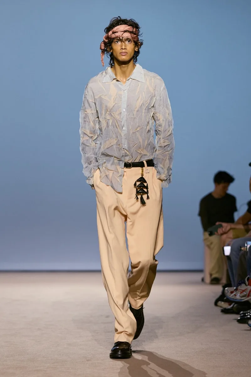 Modèle en chemise texturée et pantalon beige sur podium de mode.