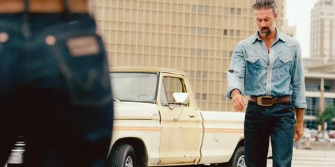 Homme en chemise denim et jeans, camion vintage beige en arrière-plan