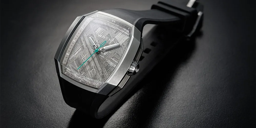 Montre moderne avec bracelet noir et cadran argenté, aiguilles vertes.