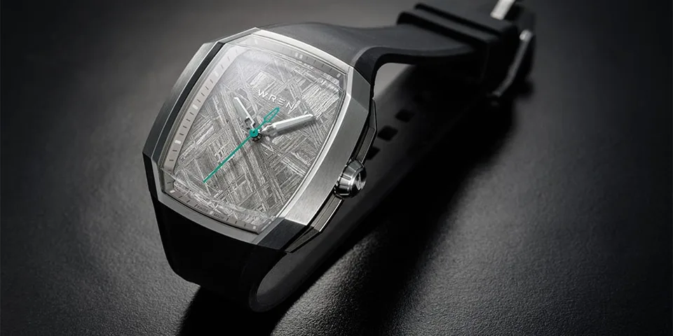 Montre moderne avec bracelet noir et cadran argenté, aiguilles vertes.
