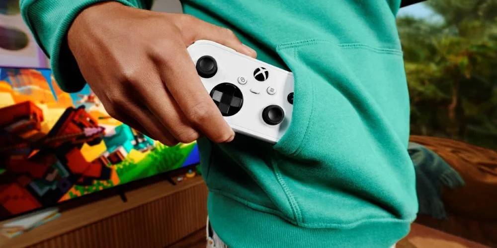 Personne tenant une manette Xbox blanche près d'un téléviseur avec jeu coloré.