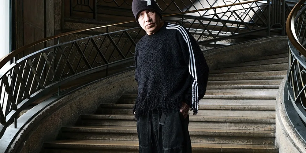 Homme en pull noir et bonnet sur escalier intérieur élégant.