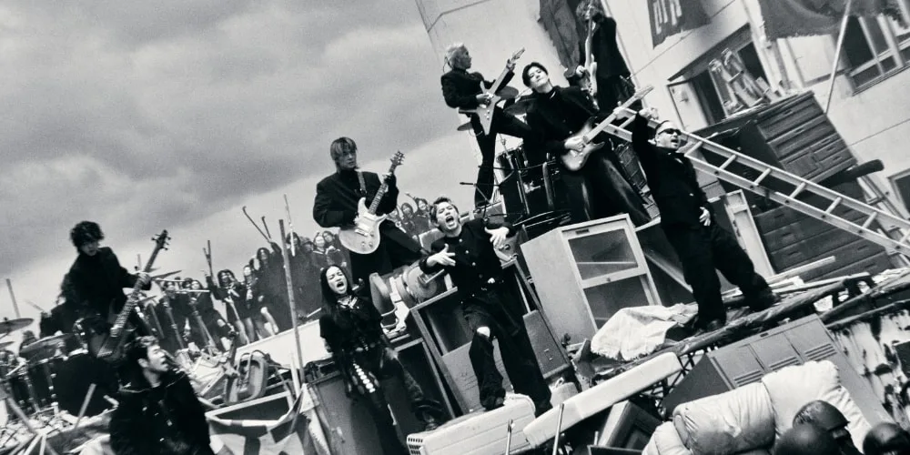 Groupe de personnes sur une scène chaotique avec des instruments de musique.