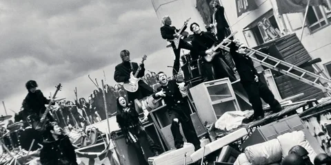 Groupe de personnes sur une scène chaotique avec des instruments de musique.