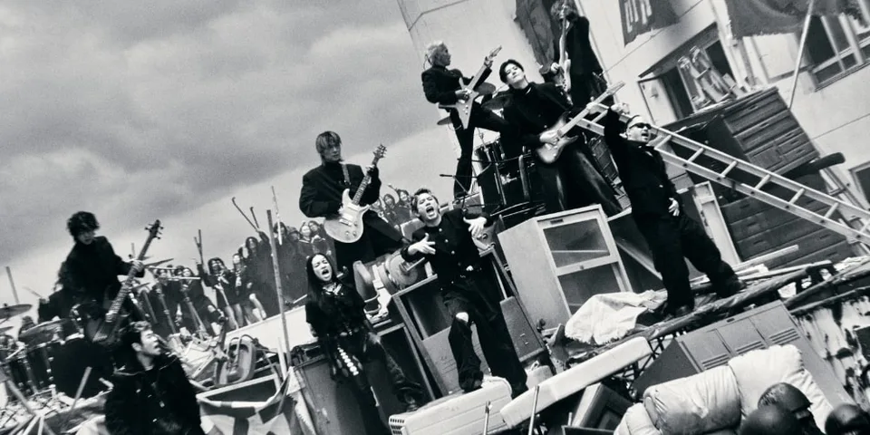 Groupe de personnes sur une scène chaotique avec des instruments de musique.
