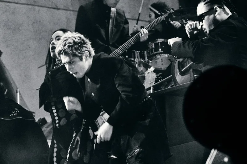Concert en noir et blanc avec artistes et instruments de musique sur scène.