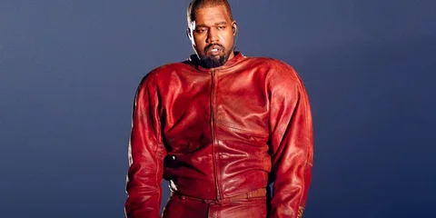 Kanye West porte une veste rouge devant un fond bleu.
