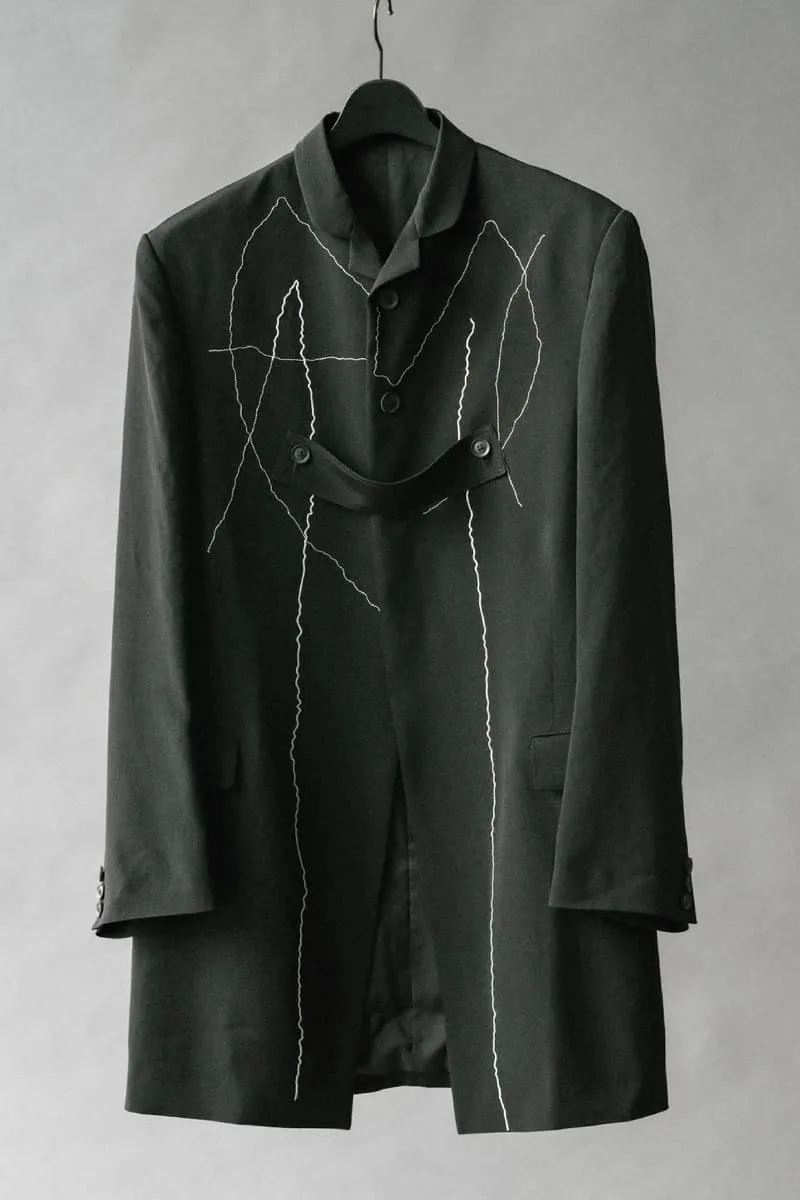 Manteau noir avec des motifs de couture blanche suspendu sur un cintre.